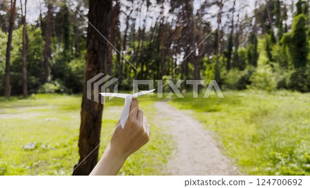 Female hand playing with paper airplane at summer forest. Girl walking with toy plane at woodland on sunny day. Young woman having fun at nature. Concept of leisure outdoor. Close up 124700692