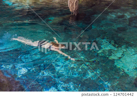Female tourist enjoying a refreshing swim in a Mexican cenote with turquoise water. Adventure, travel, and nature exploration concept Female tourist enjoying a refreshing swim in a Mexican cenote with turquoise water. Adventure, travel, and nature exploration concept 124701442