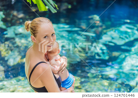 Mother with her baby standing by a Mexican cenote with turquoise water. Family adventure, travel, and nature bonding concept Mother with her baby standing by a Mexican cenote with turquoise water. Family adventure, travel, and nature bonding concept 124701446