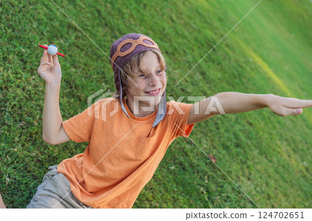 Boy wearing a pilot hat running through the grass with a toy airplane, dreaming of adventures. Childhood, imagination, and freedom concept 124702651