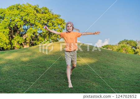 Boy wearing a pilot hat running through the grass with a toy airplane, dreaming of adventures. Childhood, imagination, and freedom concept 124702652