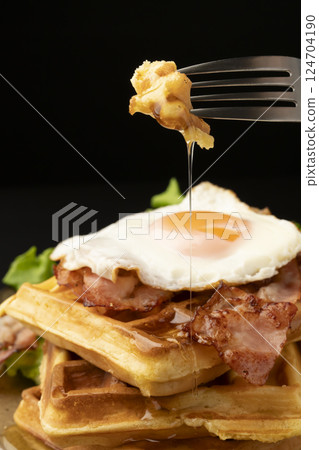 Waffles and bacon and eggs breakfast Picking up a waffle with a fork Waffles and bacon and eggs breakfast Picking up a waffle with a fork 124704190