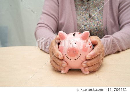 Retired elderly woman counting coins money with piggy bank and worry about monthly expenses and treatment fee payment. Retired elderly woman counting coins money with piggy bank and worry about monthly expenses and treatment fee payment. 124704581