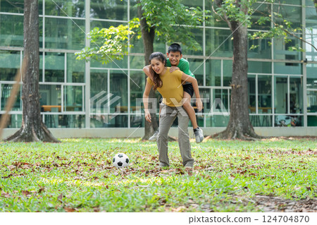 Playful Moments and Family Connection. A child enjoys being carried by his mother in a fun park setting. Playful Moments and Family Connection. A child enjoys being carried by his mother in a fun park setting. 124704870