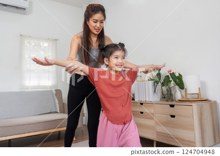 Exercise and Fitness Fun. A guiding mother helping her daughter with a stretching workout in a cozy living space. 124704948