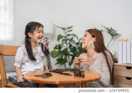 Family Fun and Bonding. A mother and daughter sharing laughter and joy while playing a domino game at home. 124704950