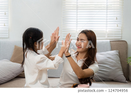 Playful Interaction and Bonding. A mother and daughter playing a hand game at home, fostering joy and connection. Playful Interaction and Bonding. A mother and daughter playing a hand game at home, fostering joy and connection. 124704956