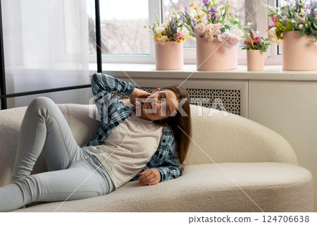 Teen girl posing casually on sofa near floral decoration. 124706638