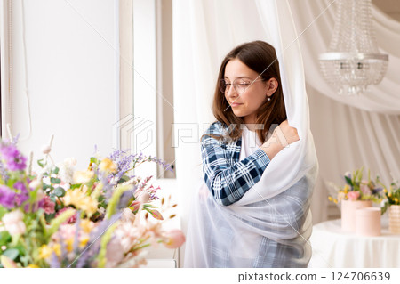 Teenage girl wrapped in sheer curtain by sunny window. 124706639