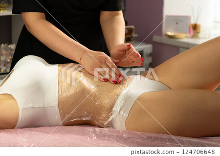 Beautician uses rhythmic hand motion on client's wrapped midsection. Beautician uses rhythmic hand motion on client's wrapped midsection. 124706648