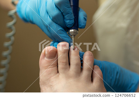 Technician shapes toenails during dry hardware pedicure with precision. Technician shapes toenails during dry hardware pedicure with precision. 124706652