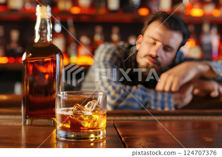 A drunk man fell asleep on the bar counter in front of an unfinished bottle of whiskey. A close-up of a man asleep at the bar, his unfinished whiskey bottle signifying a wild evening. 124707376