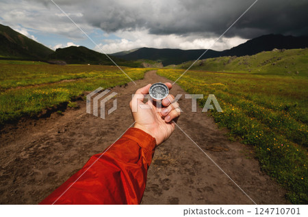Man explorer searches for direction with a compass in a green field on an off-road. A first-person view of the upcoming path through the mountains 124710701