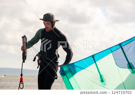 A male kitesurfer unwinds and straightens the lines of her kite before riding. Preparing the kite for kitesurfing A male kitesurfer unwinds and straightens the lines of her kite before riding. Preparing the kite for kitesurfing 124710702