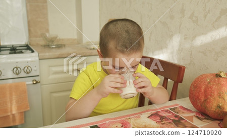 A Cheerful Child Delightfully Sipping Milk While Sitting at the Breakfast Table with a Pumpkin 124710920