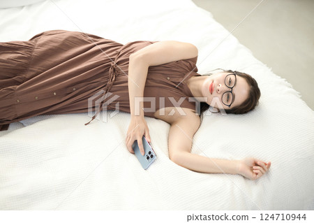 Young woman relaxing in bed and looking at her smartphone Young woman relaxing in bed and looking at her smartphone 124710944