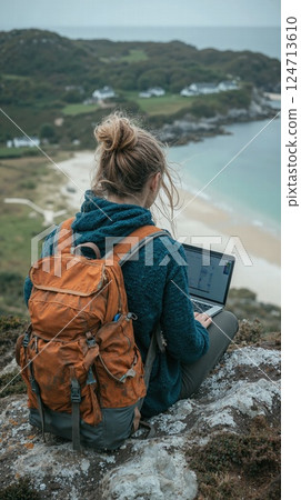 Remote work inspiration: woman with laptop on scenic clifftop overlooking coastal landscape 124713610