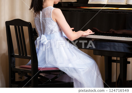 Back view of a girl wearing a dress playing the piano 124716549
