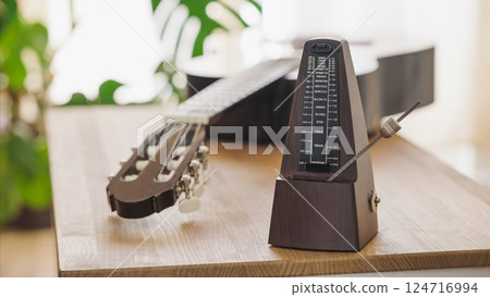 Metronome marking the tempo with classical guitar on wooden table Metronome marking the tempo with classical guitar on wooden table 124716994