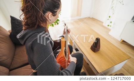 Woman playing acoustic guitar at home with metronome on table Woman playing acoustic guitar at home with metronome on table 124717000