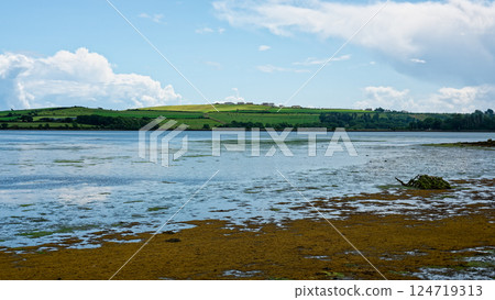 A picturesque view Inchydoney Island reveals calm waters reflecting the sky, with lush green hills in the distance. The tranquil atmosphere invites exploration and relaxation. 124719313