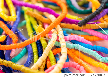 A vibrant collection of clay beads, neatly arranged by color on a white table, ready to inspire young crafters to create their own unique bracelets. 124720004