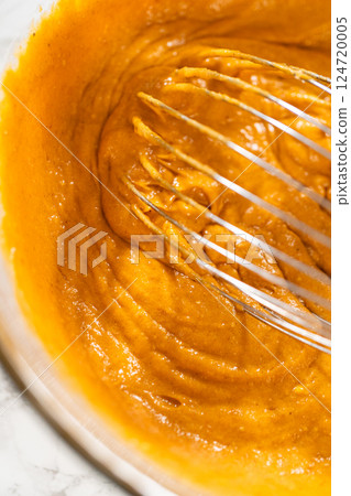 A close-up view of expertly blended ingredients in a large mixing bowl for a mouthwatering homemade pumpkin bundt cake. 124720005