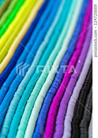 A vibrant collection of clay beads, neatly arranged by color on a white table, ready to inspire young crafters to create their own unique bracelets. 124720009