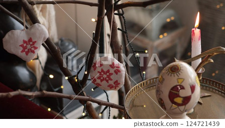 Easter handcrafted decorations displayed on a branch with warm candlelight illuminating the vibrant colors and intricate designs, creating a festive atmosphere in a cozy indoor setting Easter handcrafted decorations displayed on a branch with warm candlelight illuminating the vibrant colors and intricate designs, creating a festive atmosphere in a cozy indoor setting 124721439