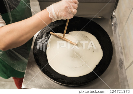 Chef prepares thin crepe in a kitchen using a flat skillet at a busy restaurant during a weekend brunch service 124721573