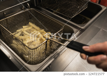 Crispy french fries being fried in a commercial kitchen during a busy lunchtime at a popular eatery 124721577
