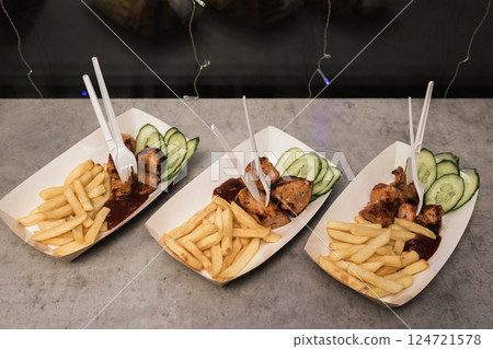 Delicious grilled chicken plates with fries and cucumber slices served at a food event in the evening Delicious grilled chicken plates with fries and cucumber slices served at a food event in the evening 124721578