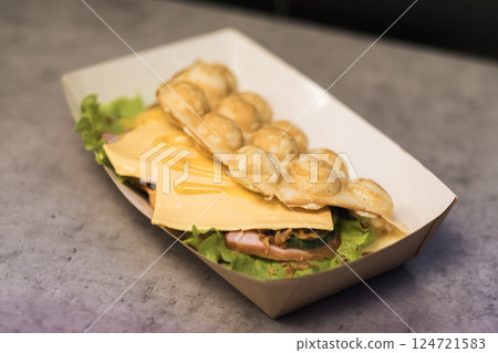 Delicious street food featuring a unique combination of fluffy egg waffles, fresh vegetables, and melted cheese served in a vibrant food stall Delicious street food featuring a unique combination of fluffy egg waffles, fresh vegetables, and melted cheese served in a vibrant food stall 124721583