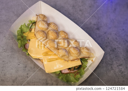 Tasty bubble waffle filled with cheese and ham served on fresh lettuce in a food market at evening hours 124721584