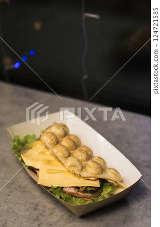 Tasty bubble waffle filled with cheese and ham served on fresh lettuce in a food market at evening hours 124721585