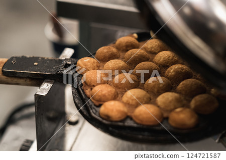 Delicious golden egg waffles being cooked in a specialized pan at a street food stall during a bustling evening market in an urban area Delicious golden egg waffles being cooked in a specialized pan at a street food stall during a bustling evening market in an urban area 124721587