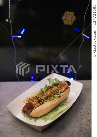 Enjoying a delicious hot dog topped with lettuce and crunchy ingredients during a festive night with twinkling lights Enjoying a delicious hot dog topped with lettuce and crunchy ingredients during a festive night with twinkling lights 124721596