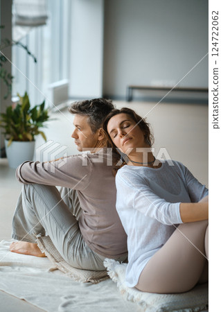 Couple engaging in mindfulness meditation practice while seated back to back in a serene indoor space during the late afternoon light 124722062