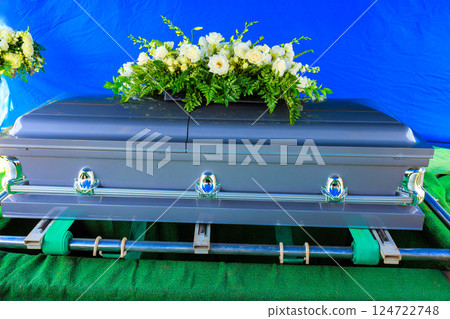 Funeral silver coffin casket with white flowers on green, creating solemn atmosphere during memorial funeral service. 124722748