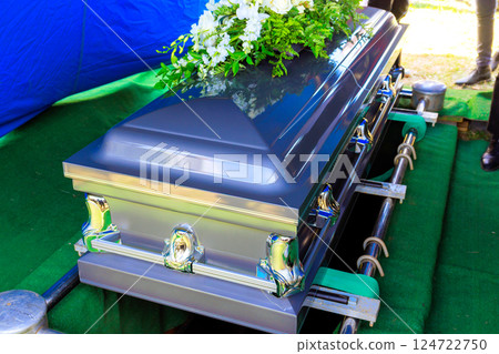 Funeral silver casket as decorated coffin is lowered at during burial ceremony. 124722750