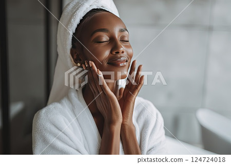 40 year old African American woman applying moisturizer to her face. Skin beauty and elasticity after 40. The woman enjoys a skincare ritual, applying a rich moisturizer to promote elasticity and glow 124724018