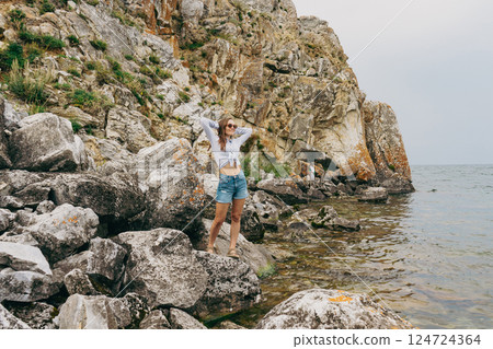 woman stands on stone, on shore of lake with rocky cliffs 124724364