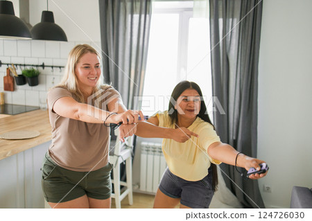 Friends having fun with drinks and snacks while playing video game at home. Two men playing video game holding joysticks while another man holds a mobile phone in hand. 124726030