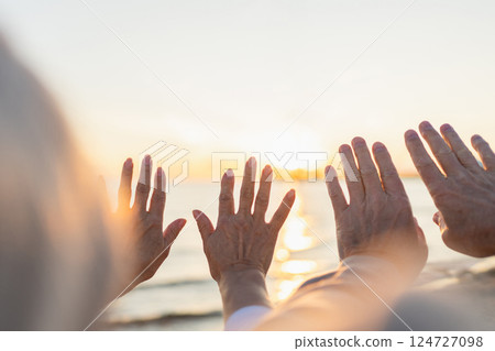 Senior couple hands at sunset. Old man woman pulls hand touching sun. Sunlight passing through fingers closeup shining sun. People stretching out hand to sun. Religion helping hand. Prayer in religion Senior couple hands at sunset. Old man woman pulls hand touching sun. Sunlight passing through fingers closeup shining sun. People stretching out hand to sun. Religion helping hand. Prayer in religion 124727098