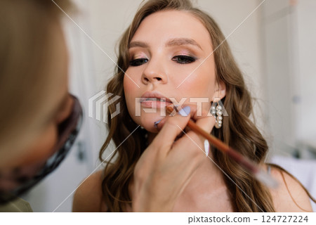 Makeup artist applies lipstick. Hand of make-up master, painting lips of young beauty model. Makeup artist applies lipstick. Hand of make-up master, painting lips of young beauty model. 124727224