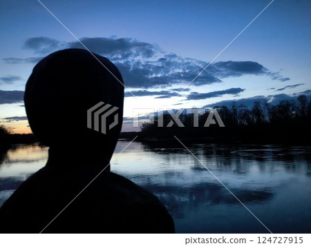Mystical sunset over the river. Silhouette of a young man against the background of a bright sunset. Nature background. purple sunset over the lake Mystical sunset over the river. Silhouette of a young man against the background of a bright sunset. Nature background. purple sunset over the lake 124727915