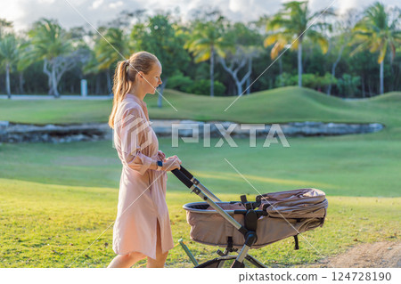 Mother walking with her baby in a stroller in the park. Peaceful outdoor bonding time. Parenthood, baby care, and family lifestyle concept 124728190