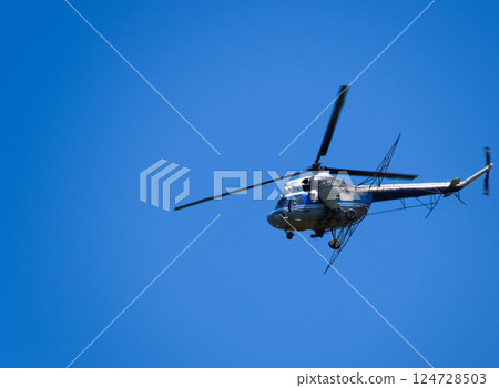 A helicopter of agricultural aviation is flying in the blue sky. 124728503