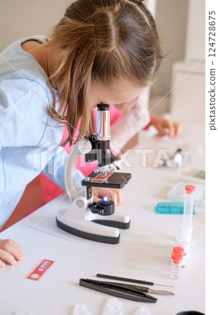 A child examines bacteria under an optical microscope. Scientific research in biology class 124728675