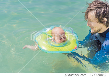 Father and newborn son swimming in the turquoise sea. Baby floating in an inflatable neck ring. Family bonding, fatherhood, and baby first water experience concept Father and newborn son swimming in the turquoise sea. Baby floating in an inflatable neck ring. Family bonding, fatherhood, and baby first water experience concept 124728832